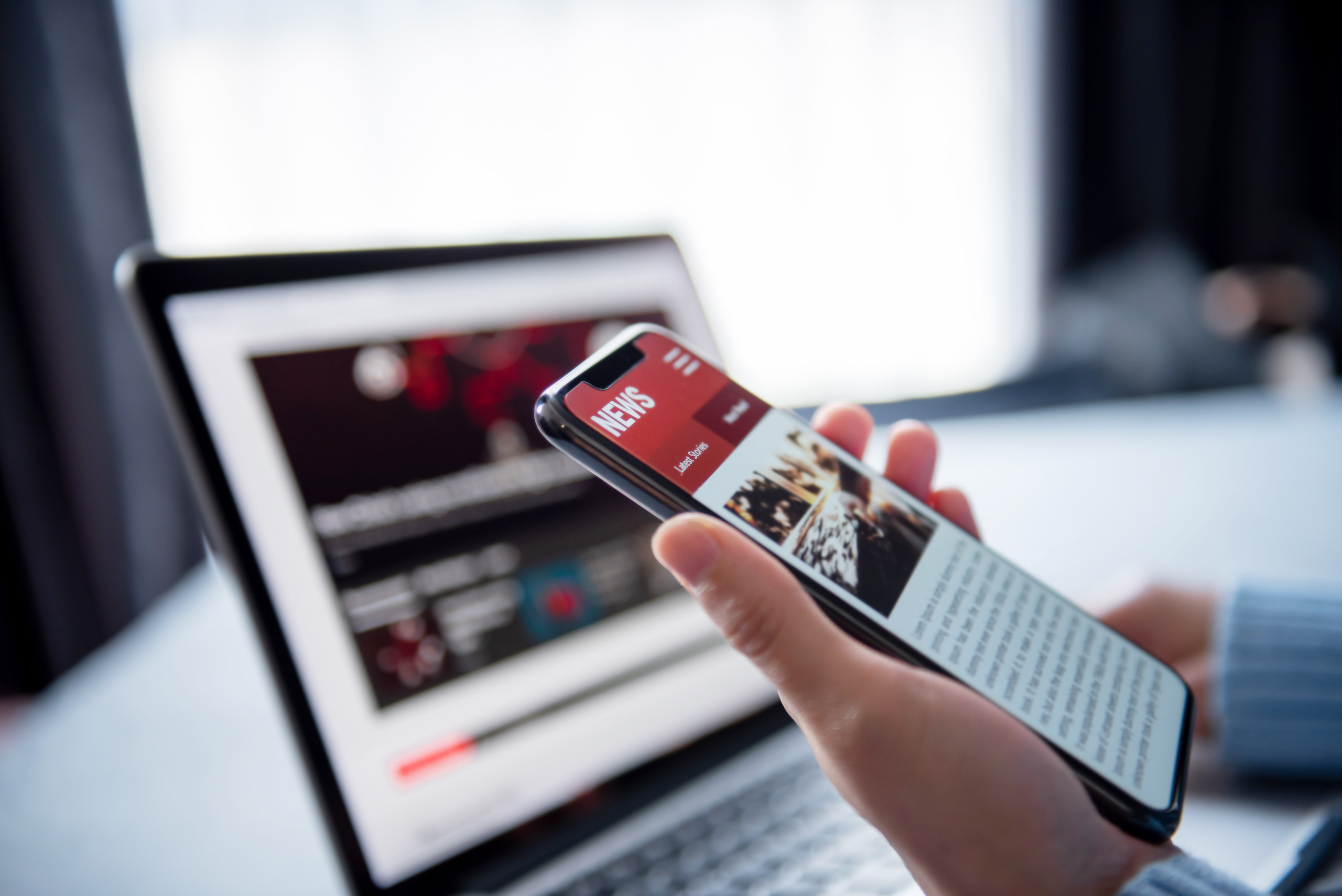 Online news on a smartphone and laptop. (Mockup website). Woman reading news or articles in a mobile phone screen application at home. Newspaper and portal on internet, copy space.