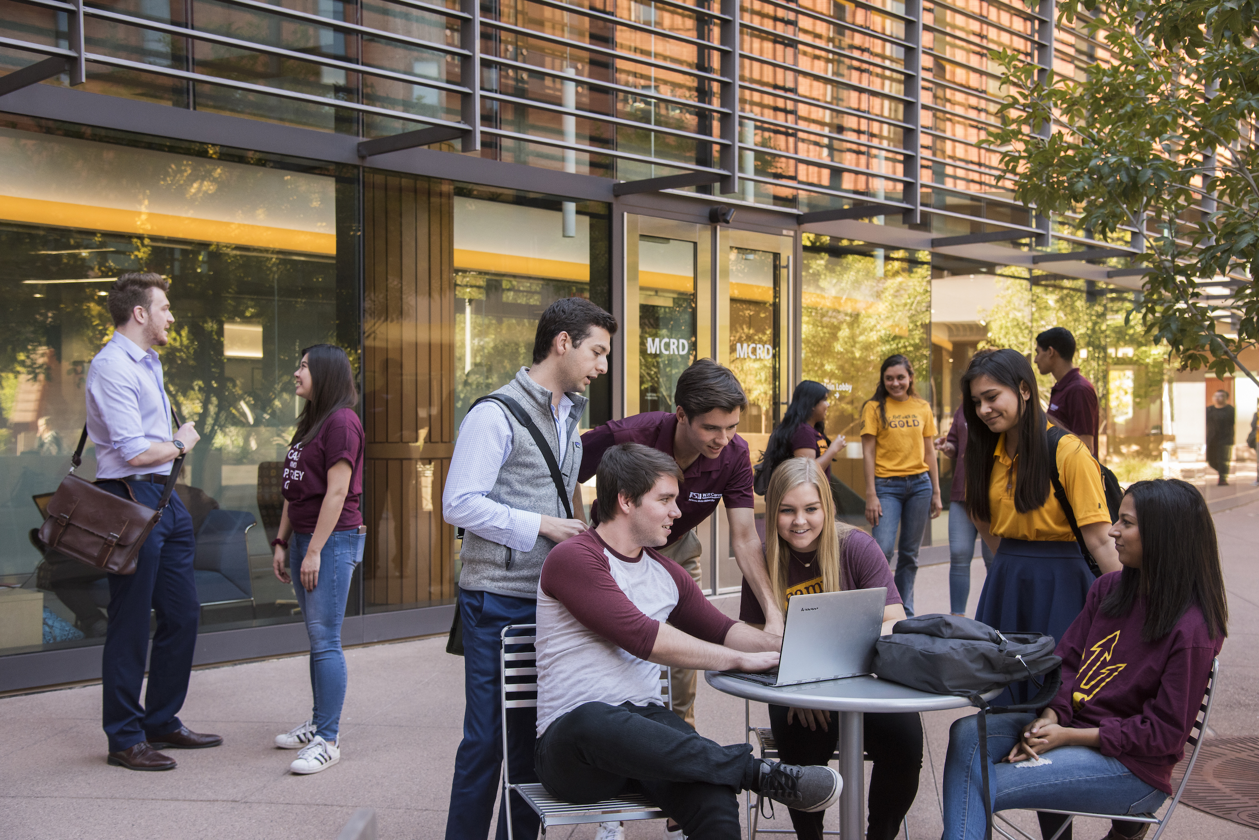 Students on patio talking at table, teacher and student talking in background