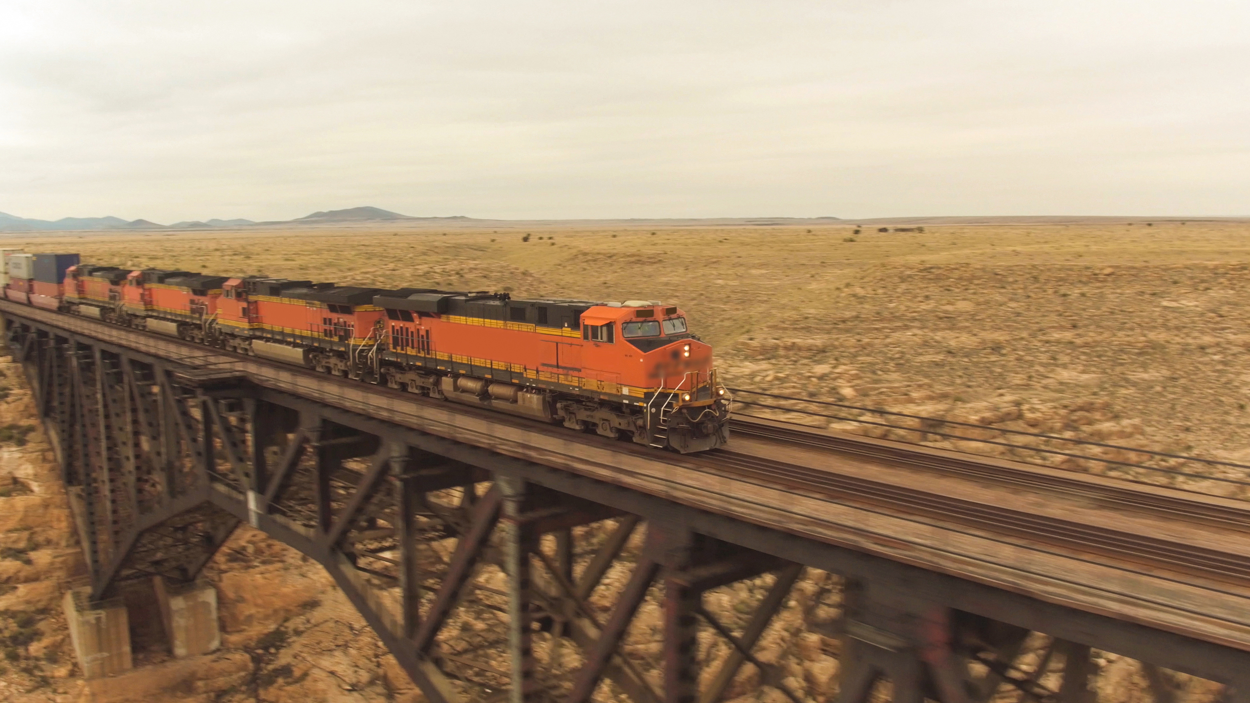 AERIAL: Container freight train crossing steel arch railroad bridge across the Canyon Diablo in the middle of the vast desert in Arizona. Rail freight transport delivering goods