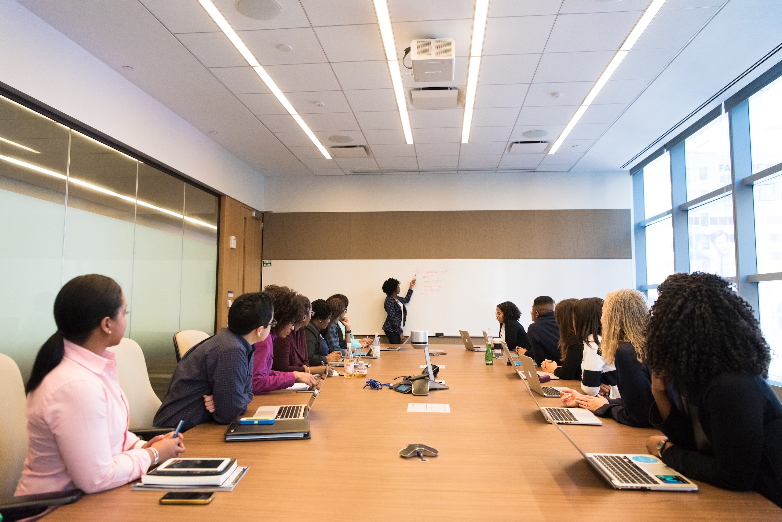 Woman at head of boardroom table writing on whiteboard