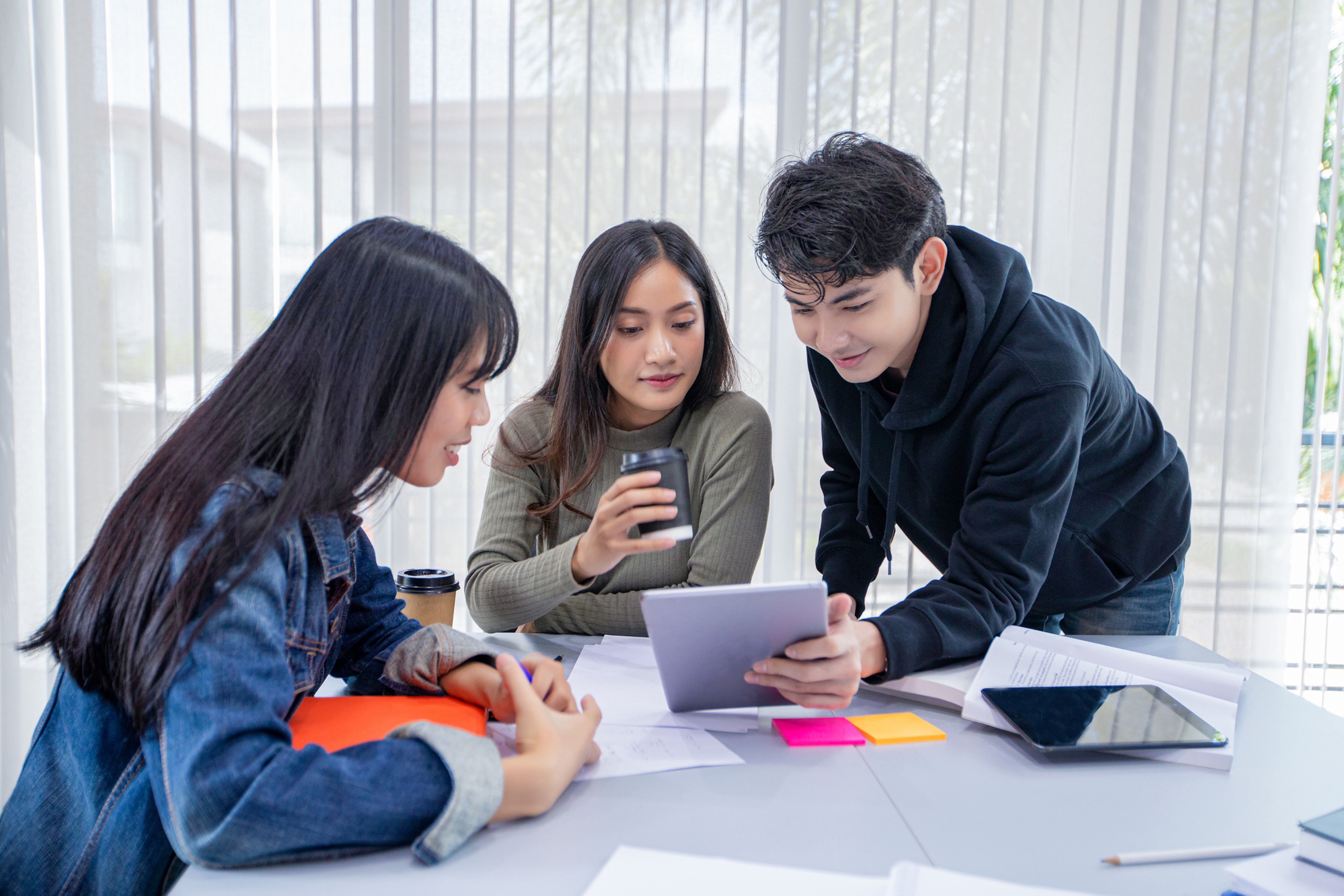 Three students gather around a desk and look at a tablet.