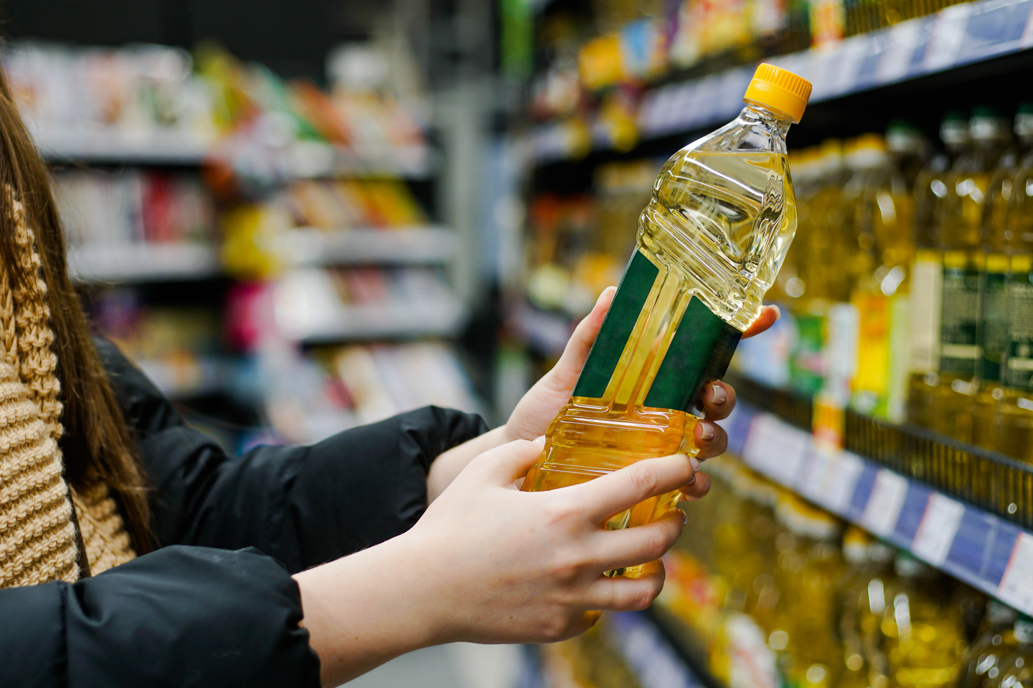 A shopper examines a bottle of oil in a grocery store aisle.