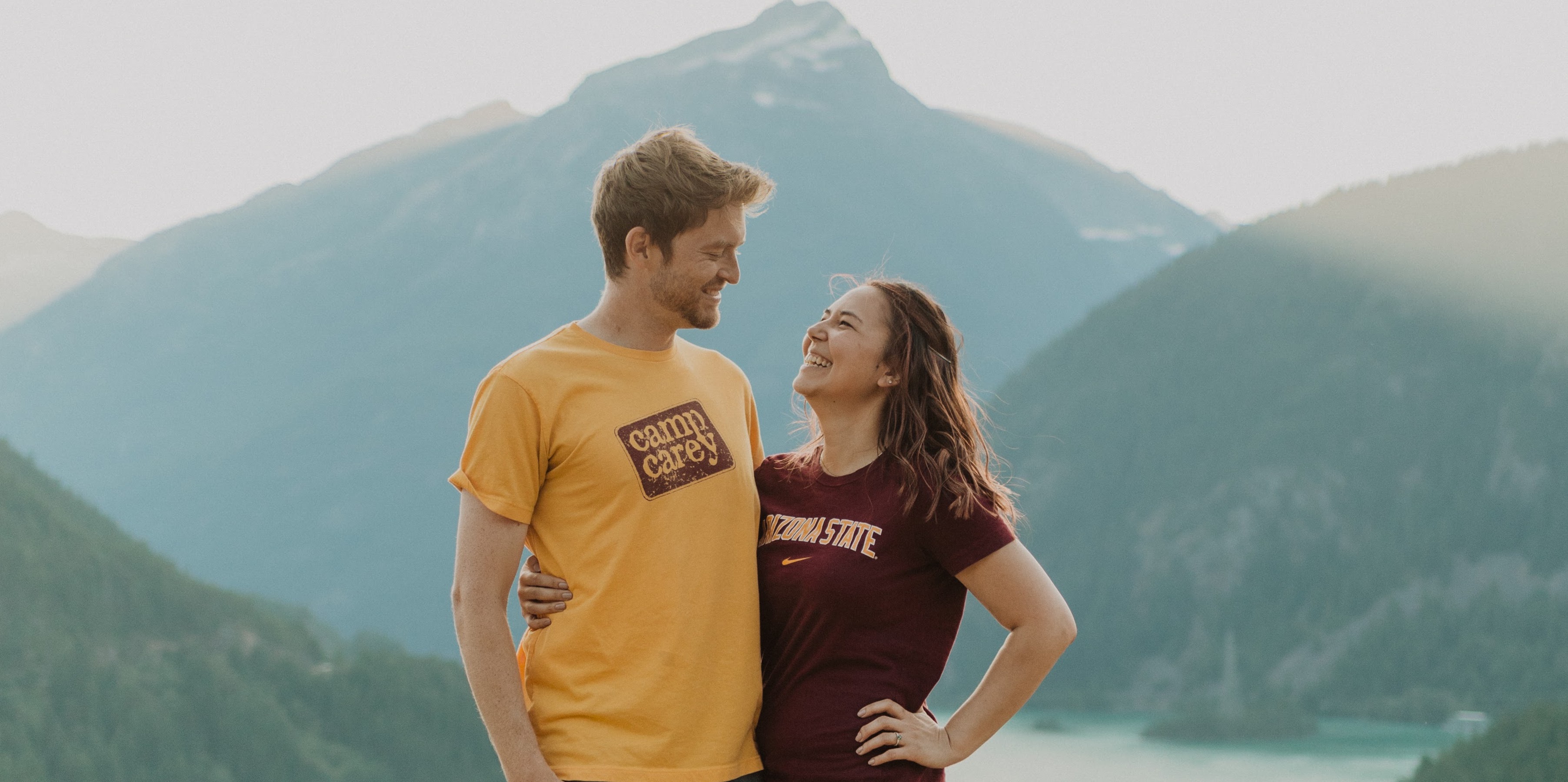 Man and woman smiling with mountain and lake in background.