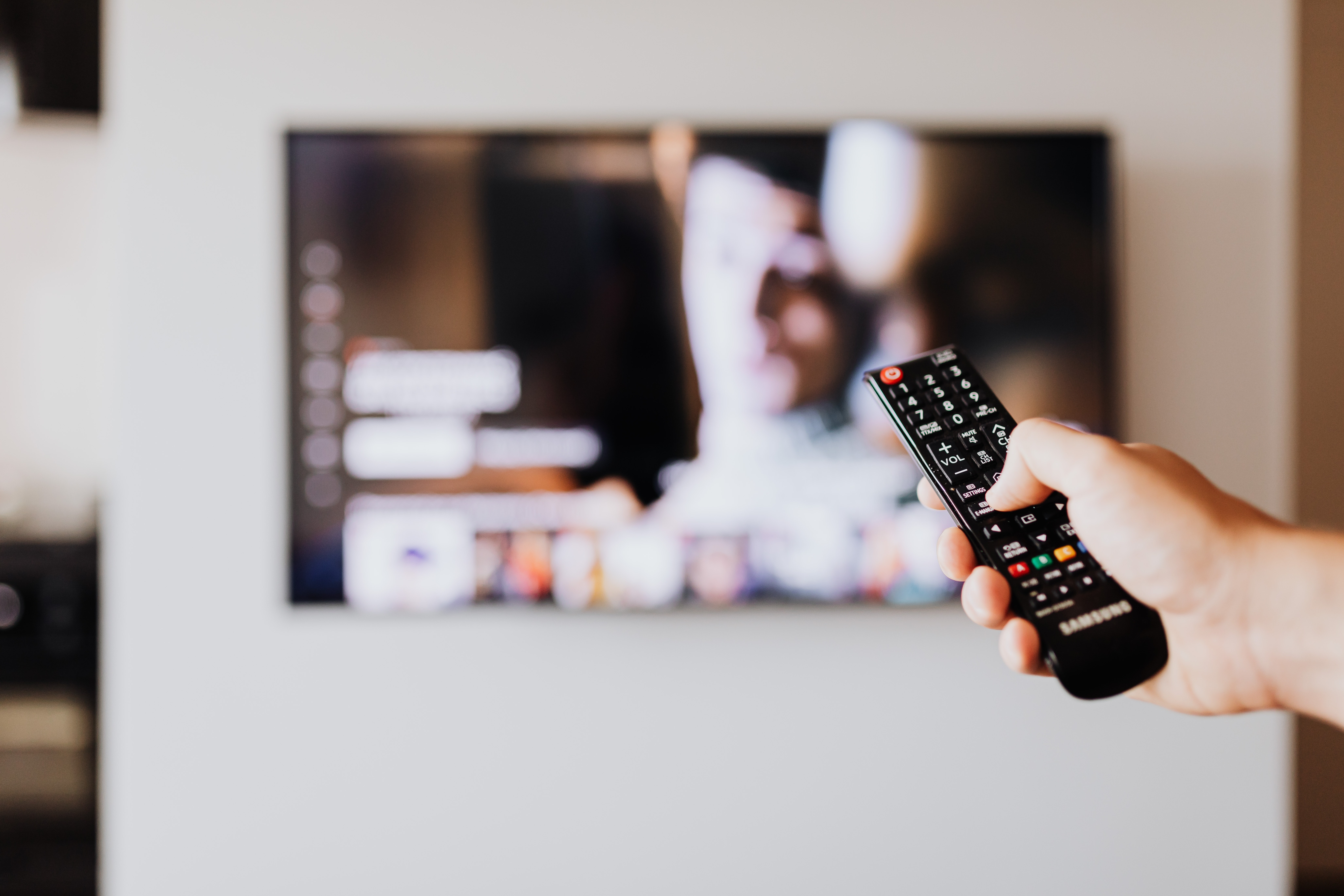 Person pointing remote at blurry TV.