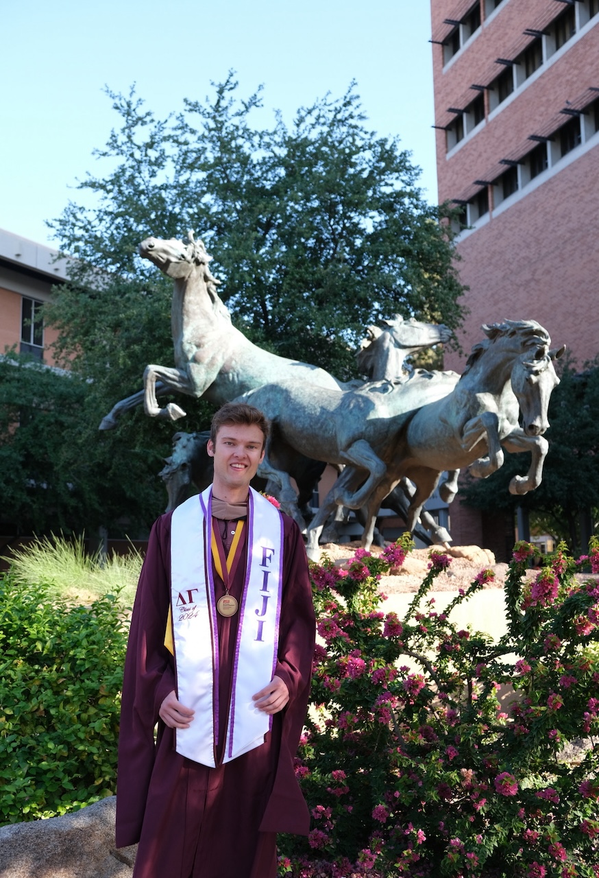 MS-FIN alumnus Carson Roland in his graduation gear by the Spirit statue