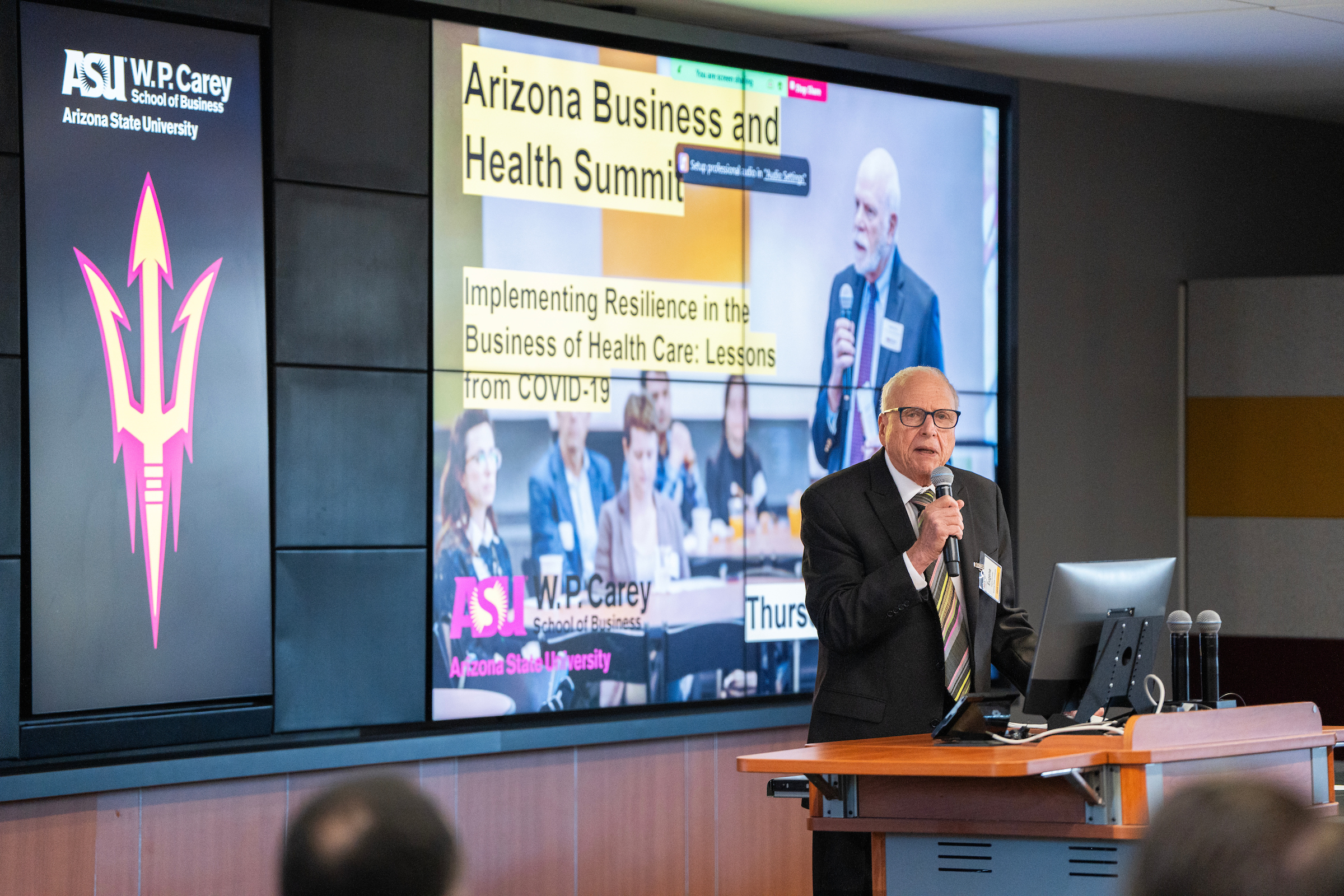 Professor Gene Schneller stands near a lectern while presenting at the 2023 Business and Health Summit