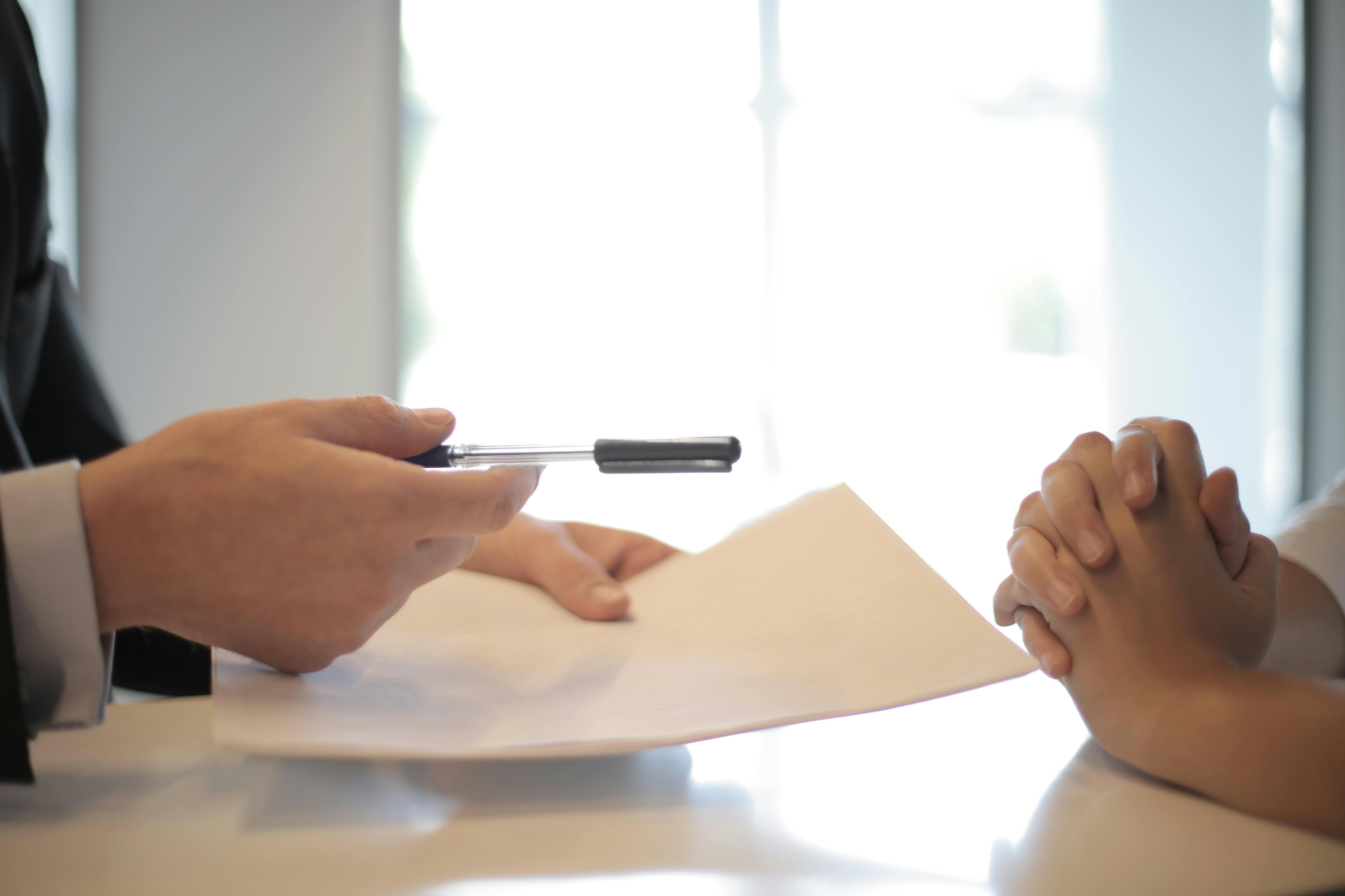 Person handing paper and pen to another person.