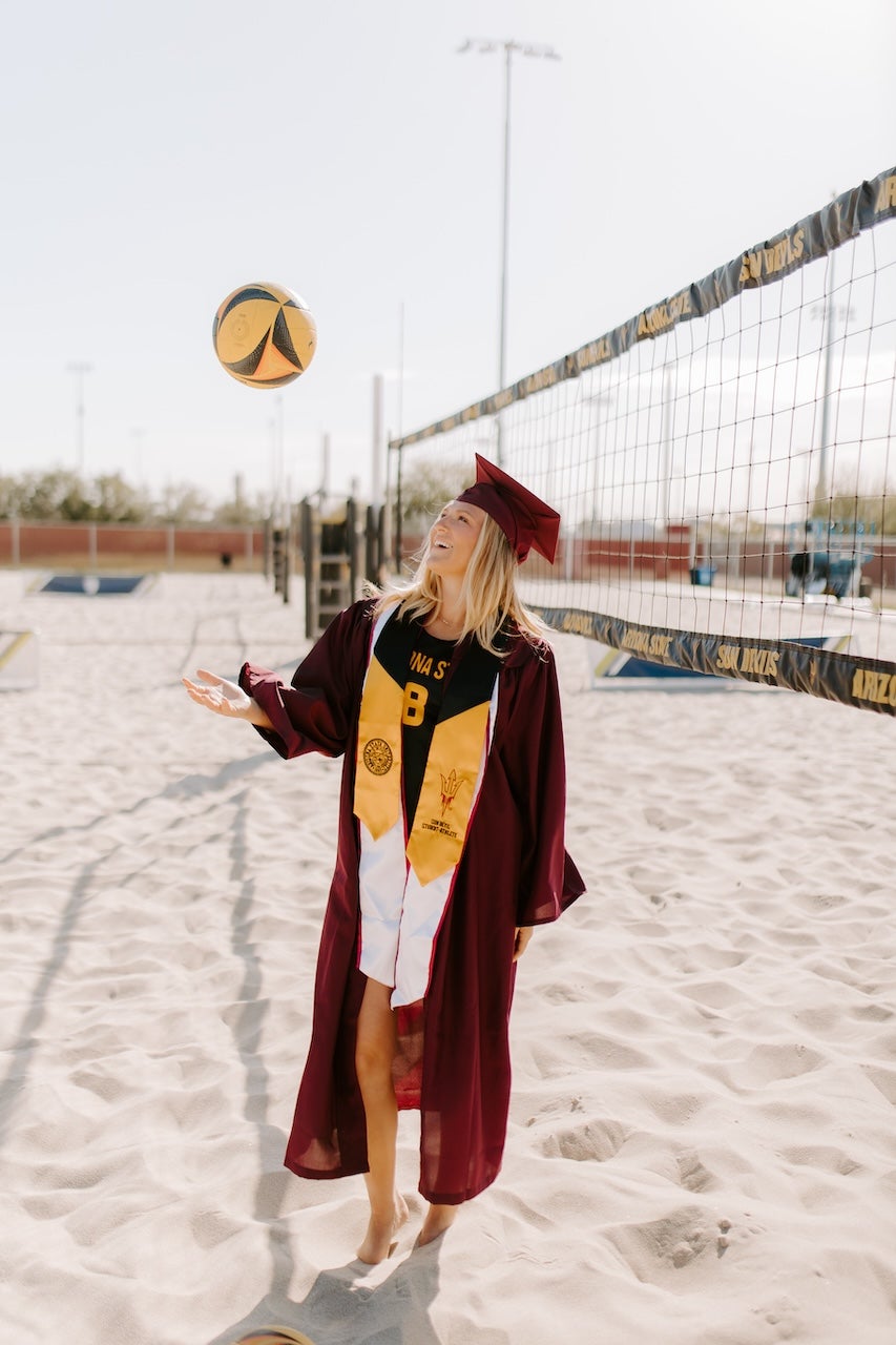 MS-EI student Kate Fitzgerald posing in her graduation gear on a beach volleyball court