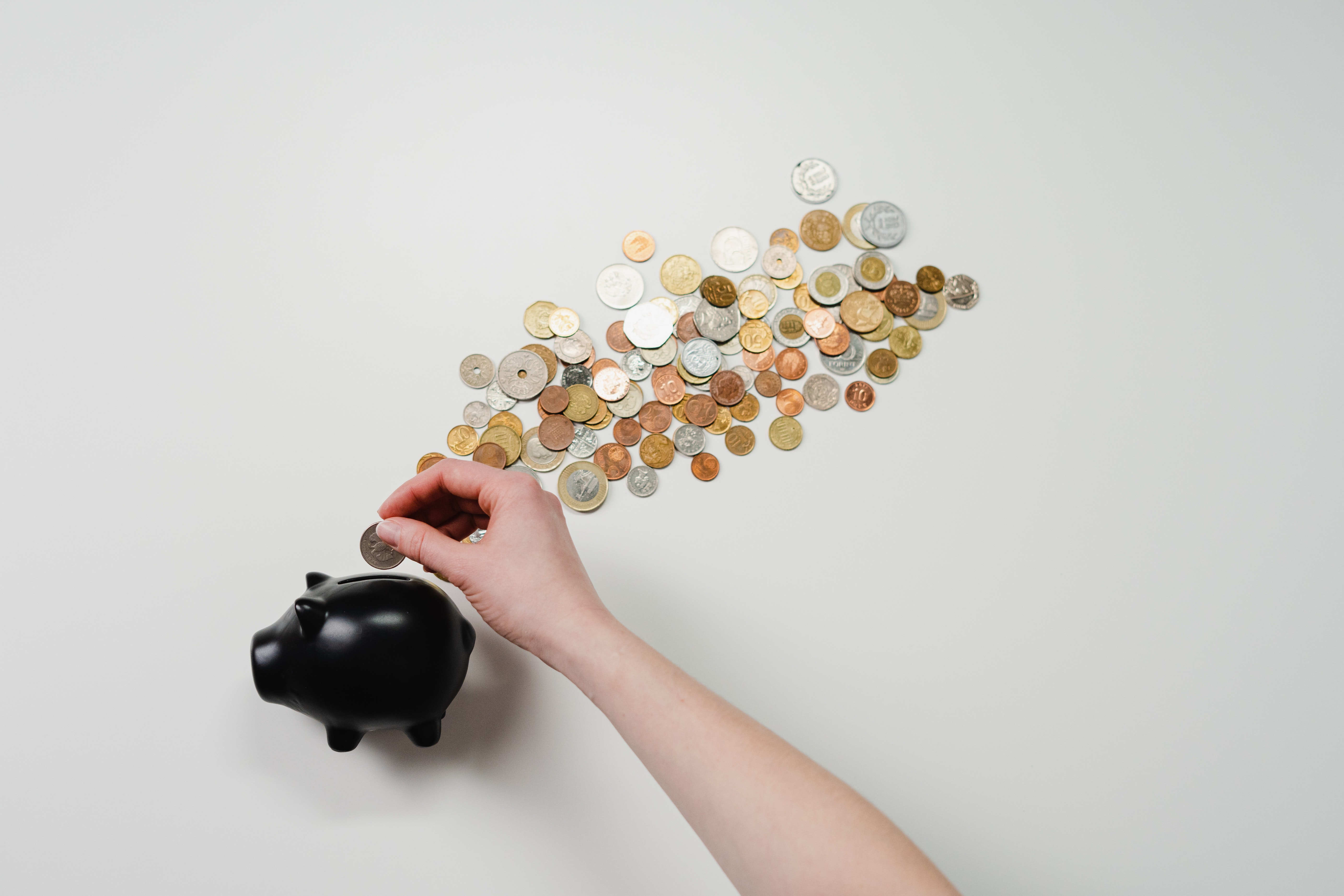 A hand places coins in a black piggy bank.