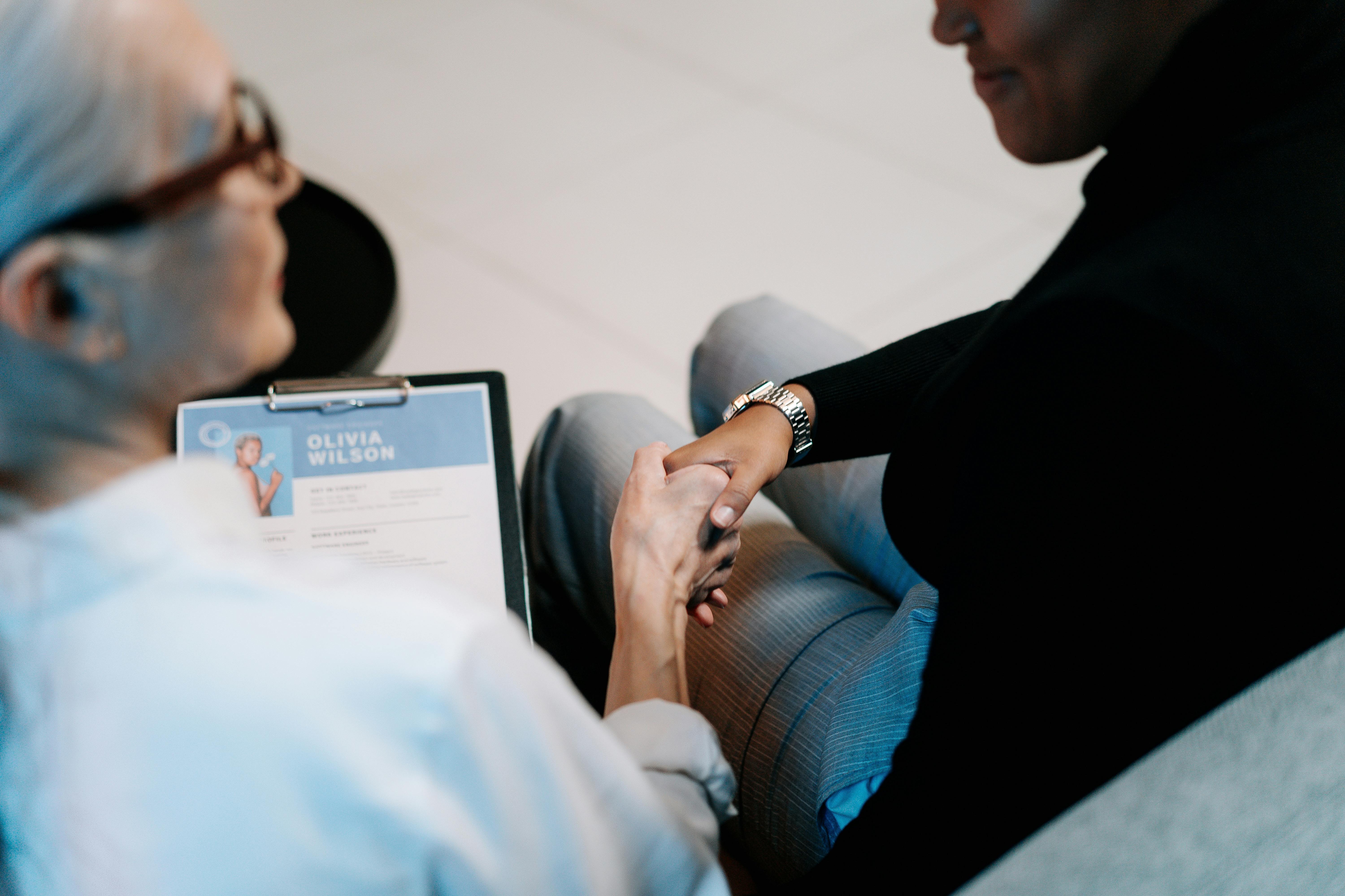 Two people shaking hands holding resume.
