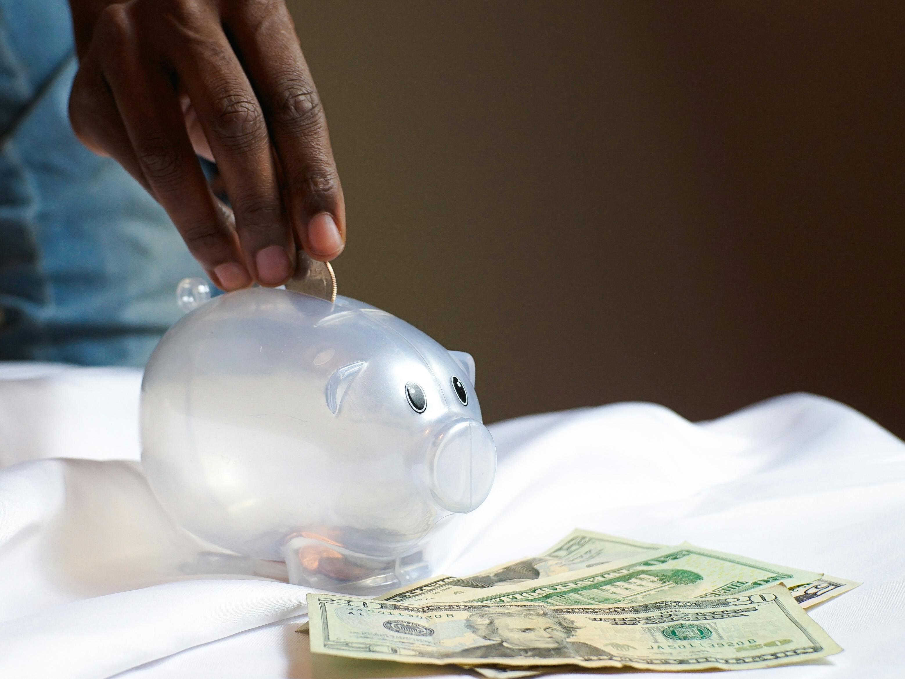 Person putting coins in a piggy bank.