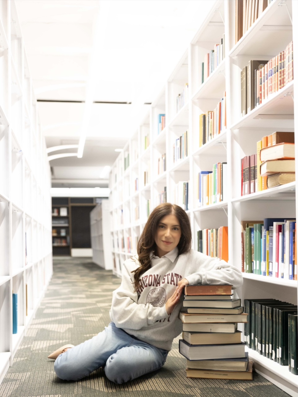 Online MACC graduate Natalie Goudarzian leans against a stack of books in a library