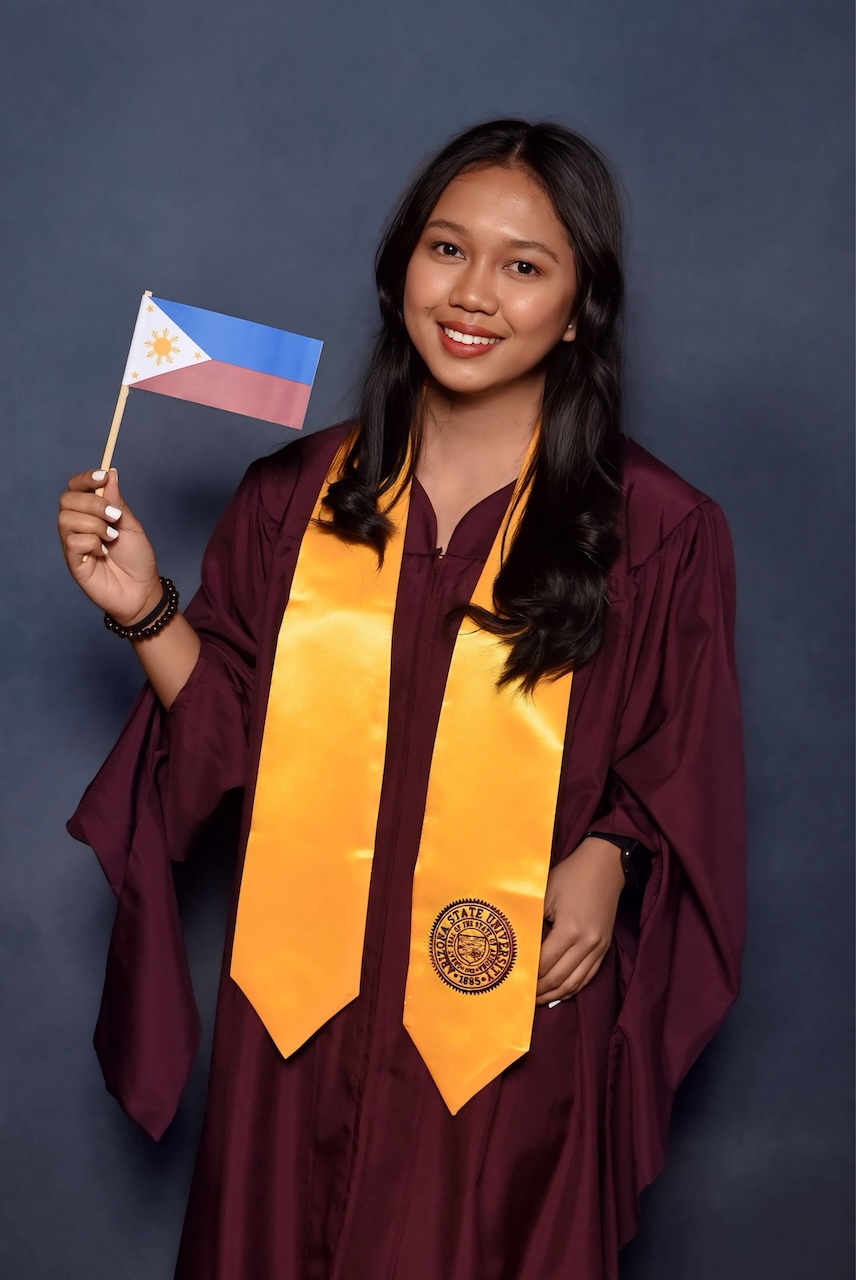 MACC graduate Shaira Catli holds a small Filipino flag while posing for a graduation photo