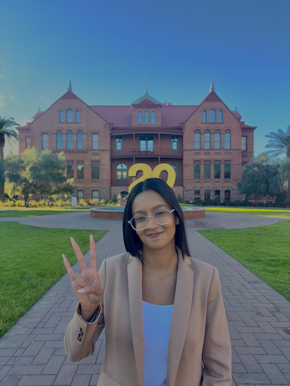Business data analytics alum Paridhi Saboo poses with a pitchfork hand symbol in front of an ASU graduation sign
